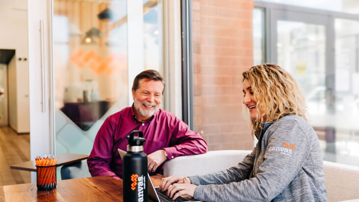 Canvas employee and a man smiling while looking down at a computer